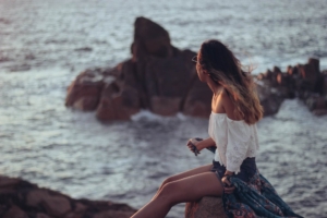 Woman sitting in rocks looking over ocean. When you're ready to begin therapy in southlake, tx, The Well House Counselors are here to help. Begin young adult therapy in Southlake, TX today for relief with anxiety, depression, or life transitions. 