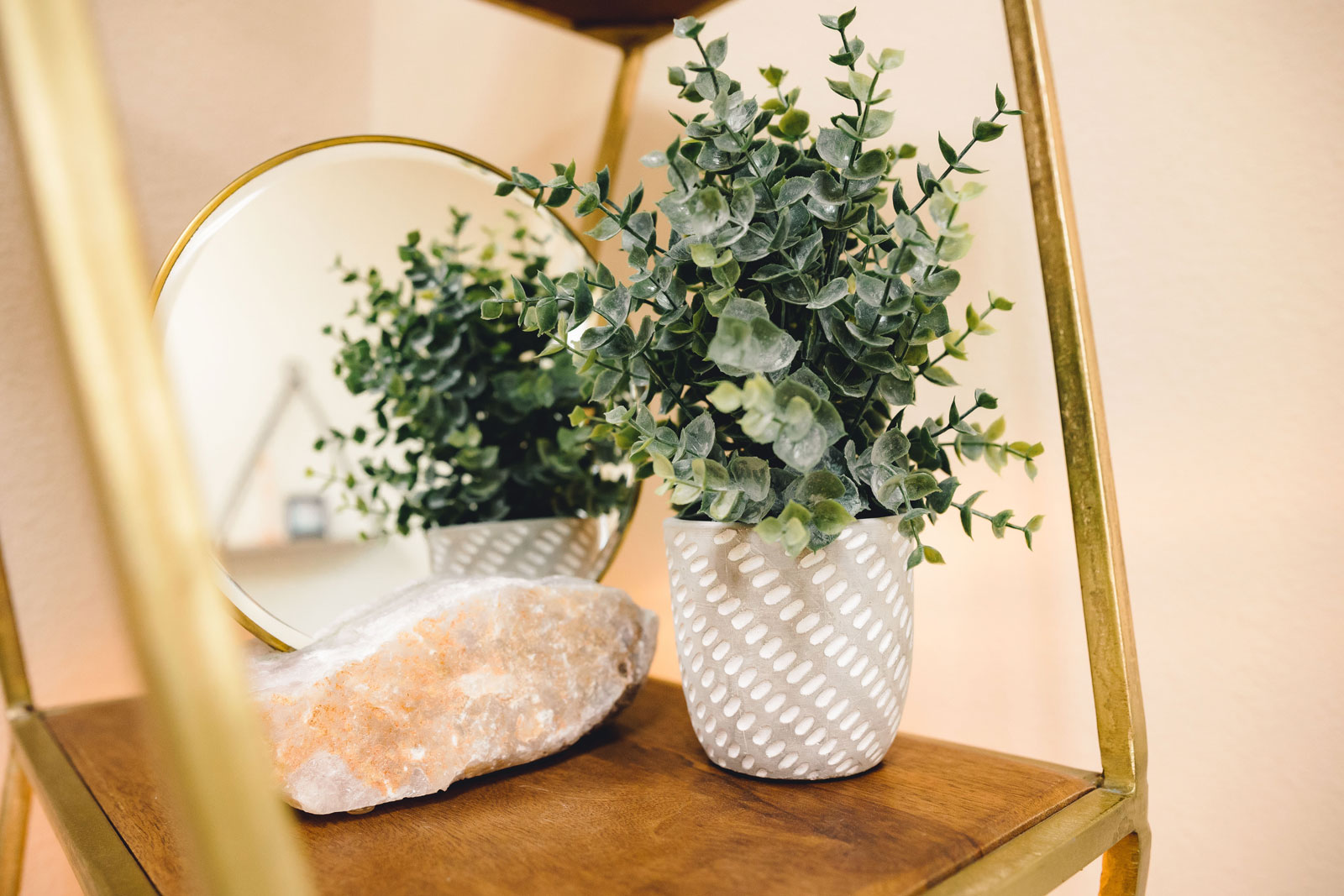 Decorative potted plant and crystal rock placed on a wooden shelf beside a round mirror with a gold frame